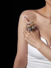 A woman's shoulder and arm elegantly showcase the CAMELLIA Virgo Flower Ring against a black background. Adorned with preserved flowers, the adjustable ring complements her white strapless top, highlighting its floral elegance.
